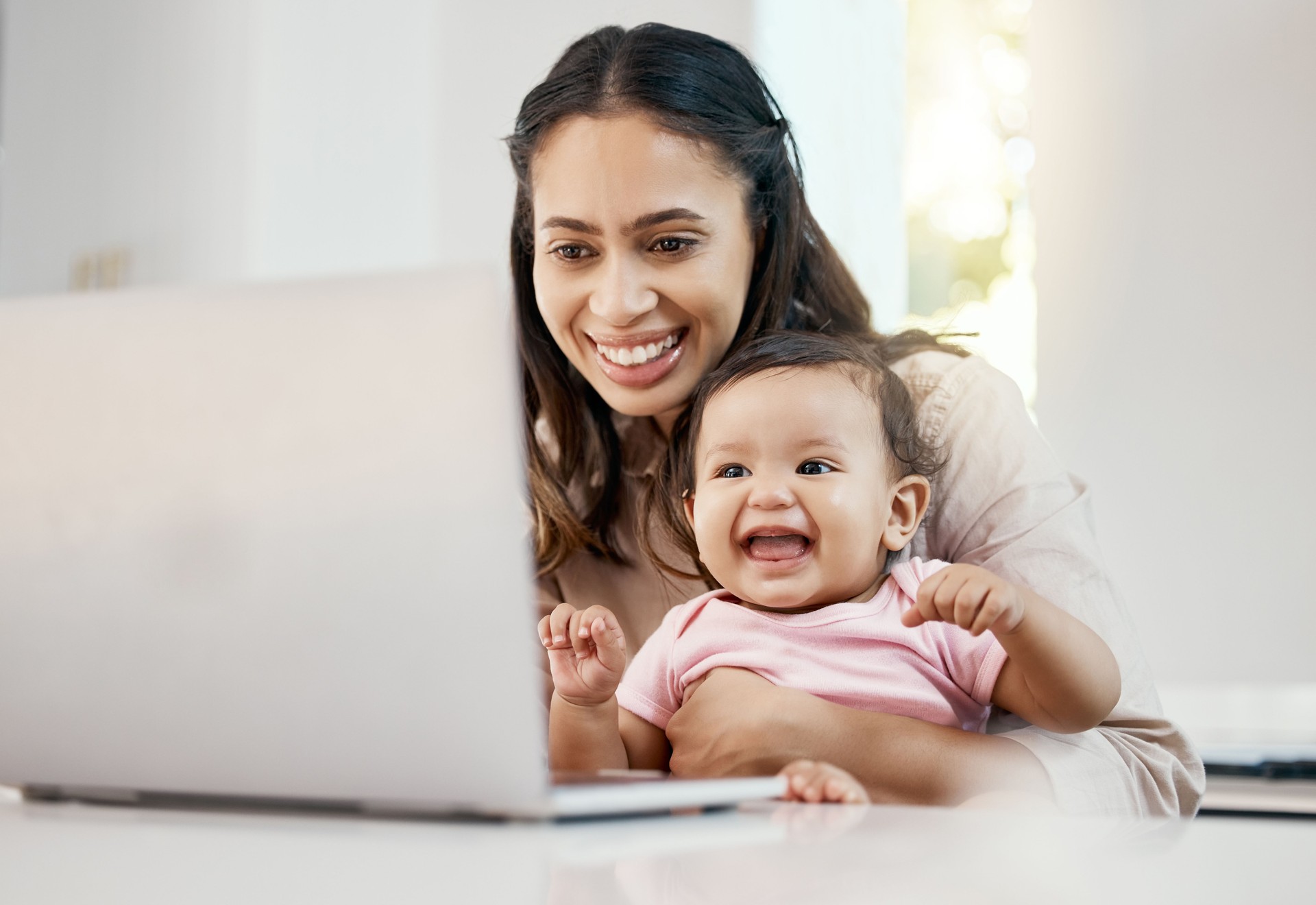 Shot of a woman working on her laptop while sitting with her baby on her lap