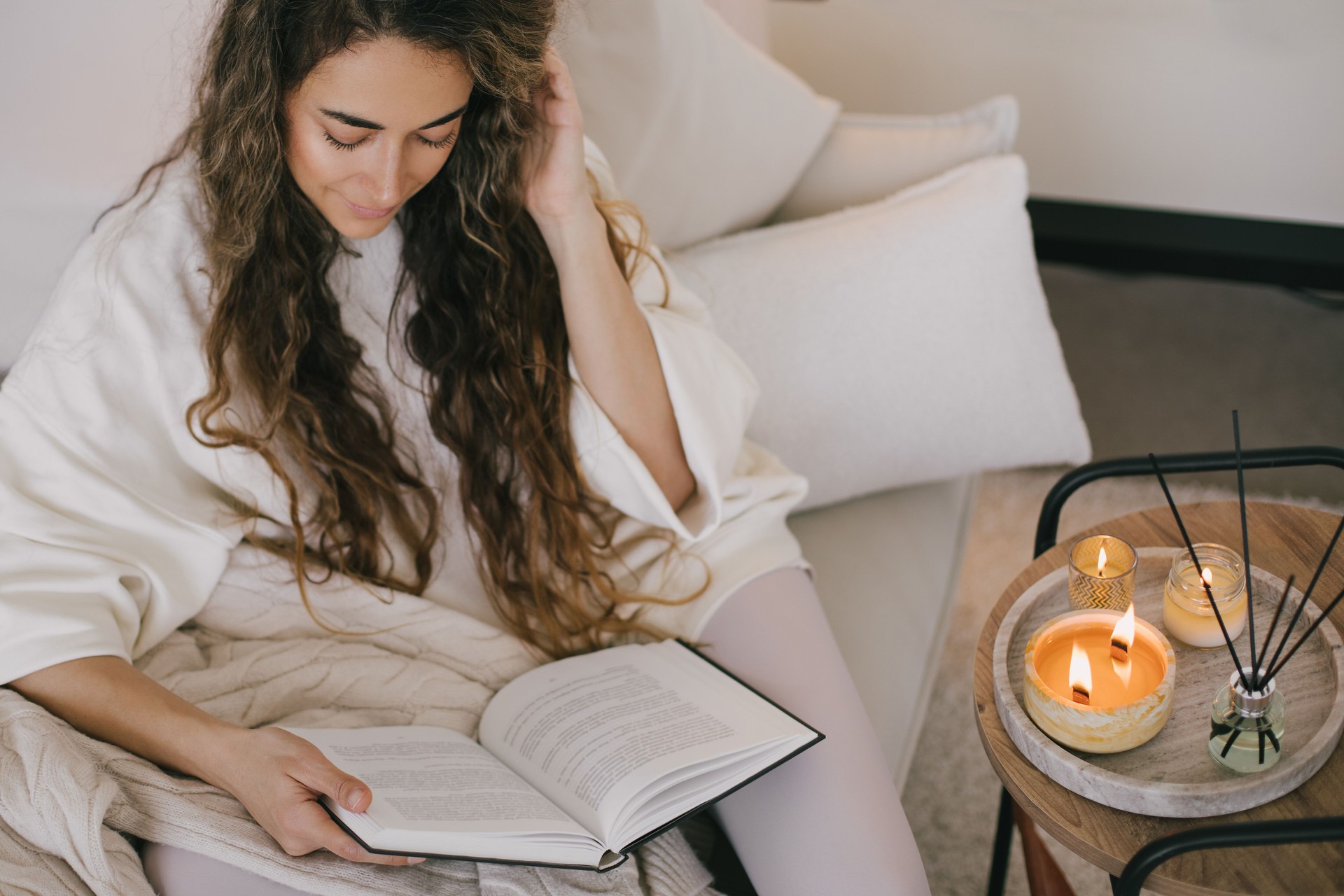 Young woman reading book and drinking tea, sitting on sofa in a cozy living room.
